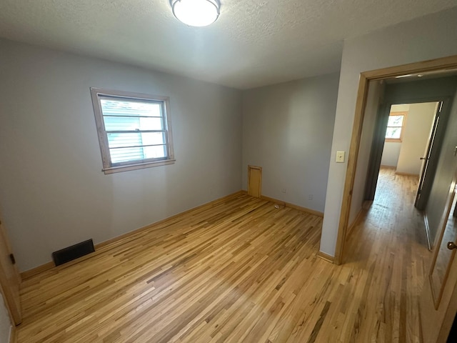 spare room with light wood-style floors, healthy amount of natural light, a textured ceiling, and baseboards