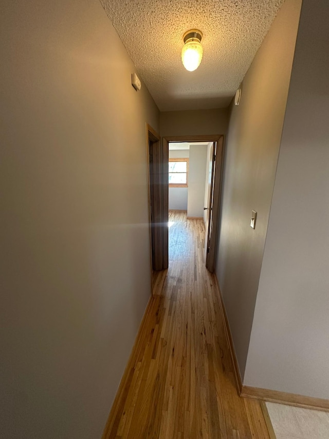 hallway with a textured ceiling, wood finished floors, and baseboards
