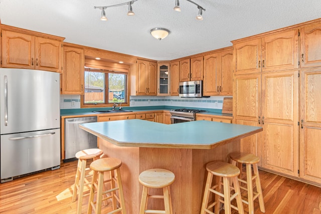 kitchen with stainless steel appliances, a sink, a kitchen bar, and light wood-style flooring