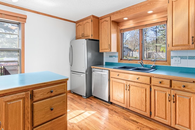 kitchen with stainless steel appliances, a sink, plenty of natural light, light wood-type flooring, and crown molding