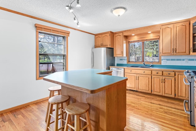 kitchen with stainless steel appliances, a sink, light wood-style floors, a breakfast bar area, and backsplash