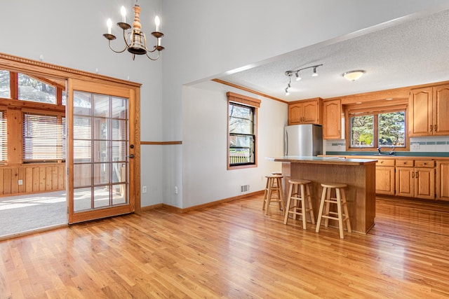 kitchen with freestanding refrigerator, a center island, light wood-type flooring, a chandelier, and a kitchen breakfast bar