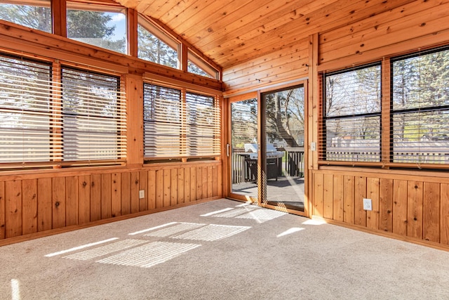 unfurnished sunroom with wood walls, vaulted ceiling, carpet flooring, and baseboards