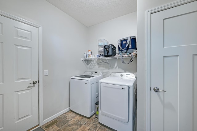 laundry area with separate washer and dryer, baseboards, a textured ceiling, and stone finish floors