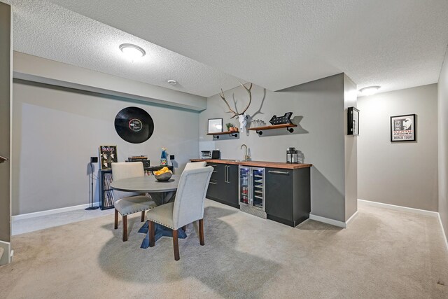 dining space featuring wet bar, beverage cooler, light colored carpet, a textured ceiling, and baseboards