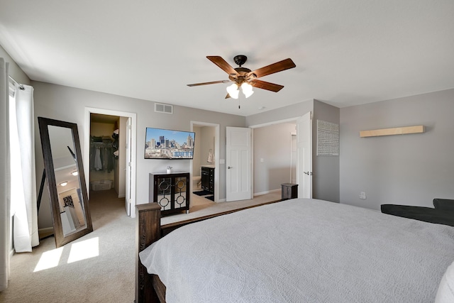 bedroom with light colored carpet, a walk in closet, a ceiling fan, a closet, and ensuite bath