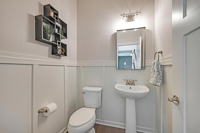 bathroom with toilet, a decorative wall, and wood finished floors