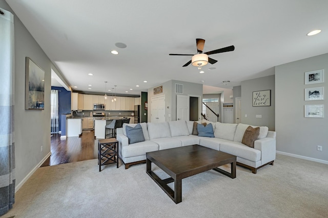 carpeted living room featuring baseboards, a ceiling fan, recessed lighting, stairs, and a sink