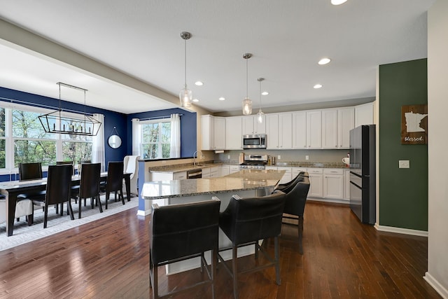 kitchen featuring appliances with stainless steel finishes, light stone countertops, white cabinetry, dark wood-style floors, and a chandelier