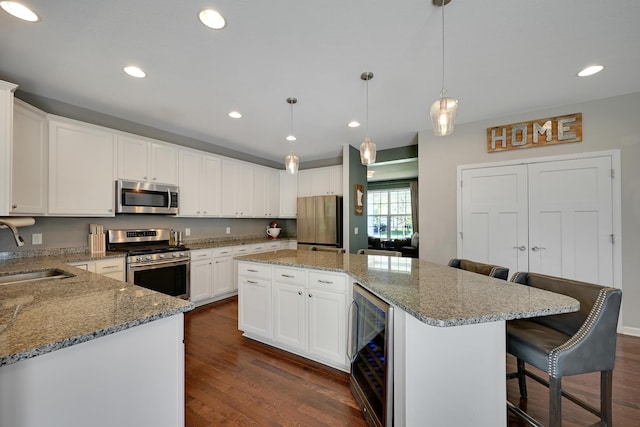 kitchen with appliances with stainless steel finishes, a sink, beverage cooler, dark wood-type flooring, and a center island