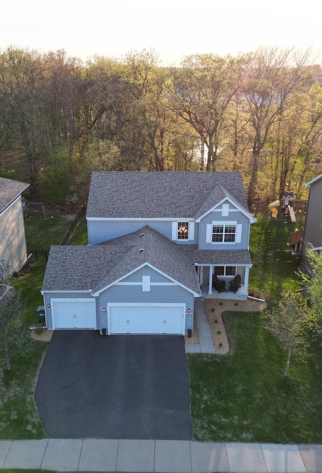 traditional-style home with asphalt driveway, a garage, roof with shingles, and a front lawn
