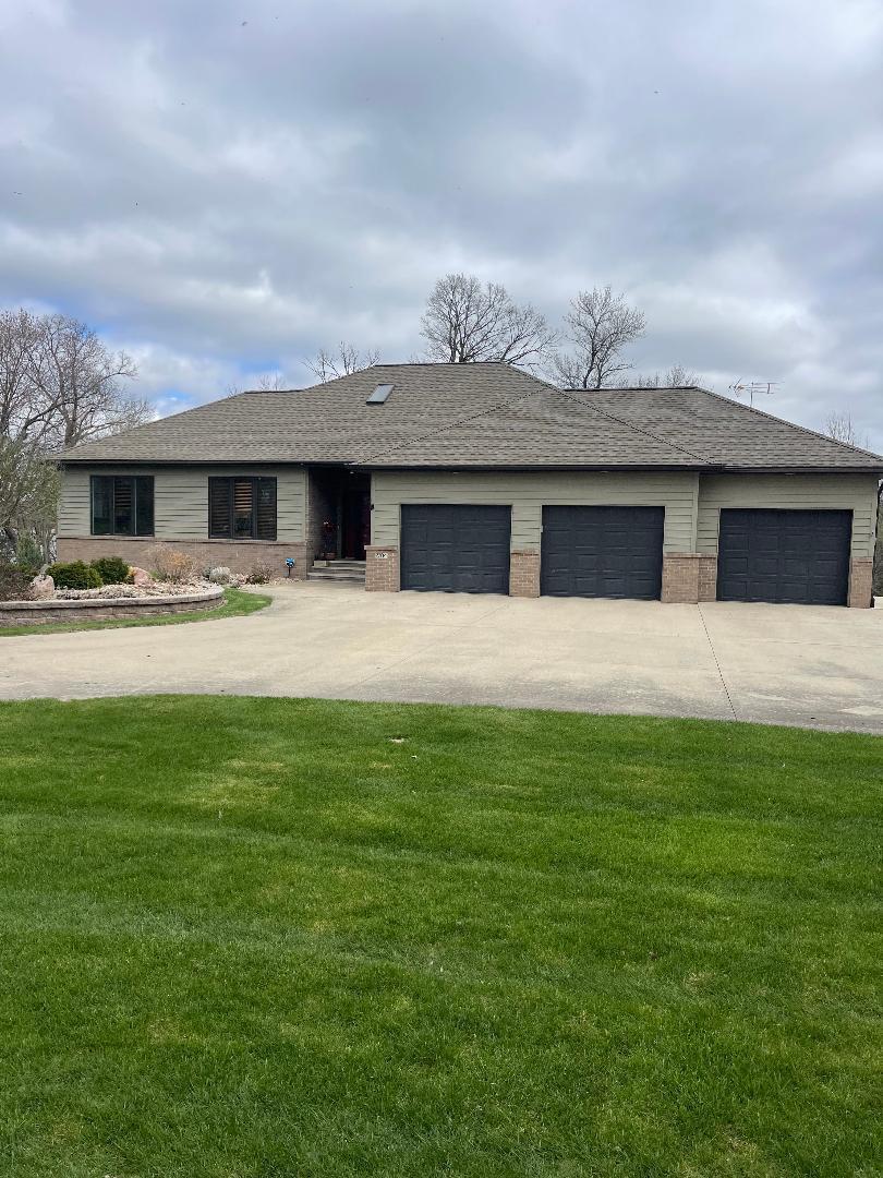 ranch-style home with driveway, brick siding, an attached garage, a shingled roof, and a front yard