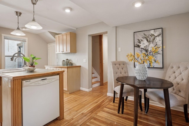 kitchen featuring white dishwasher, a sink, light wood-style floors, a center island with sink, and light countertops