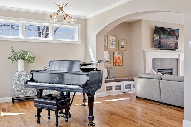living area featuring ornamental molding, an inviting chandelier, wood finished floors, arched walkways, and a tile fireplace