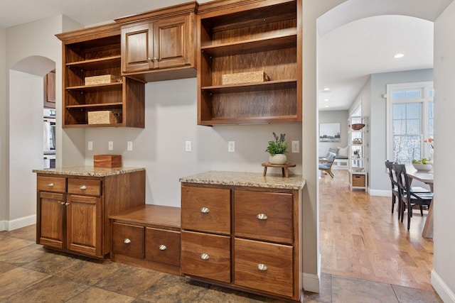 kitchen with light stone countertops, open shelves, arched walkways, and baseboards