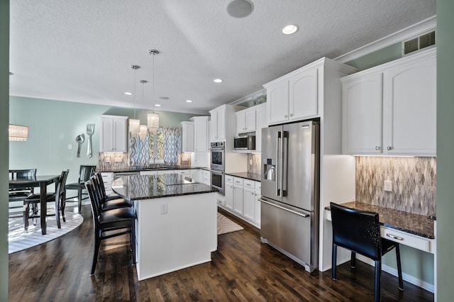 kitchen featuring stainless steel appliances, a textured ceiling, white cabinetry, backsplash, and a center island