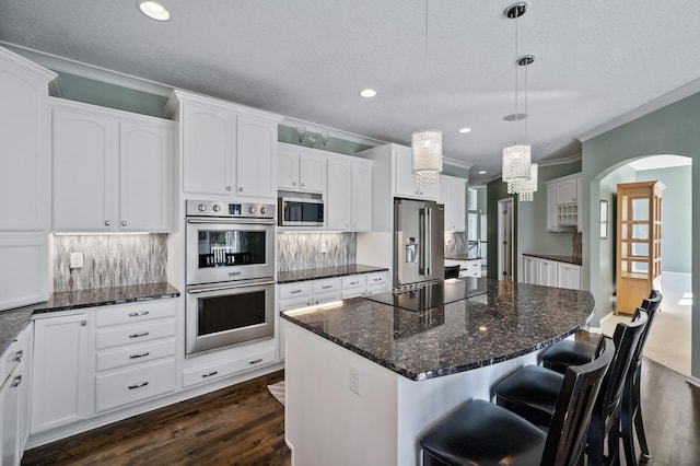 kitchen featuring dark wood-type flooring, crown molding, a kitchen island, stainless steel appliances, and white cabinets