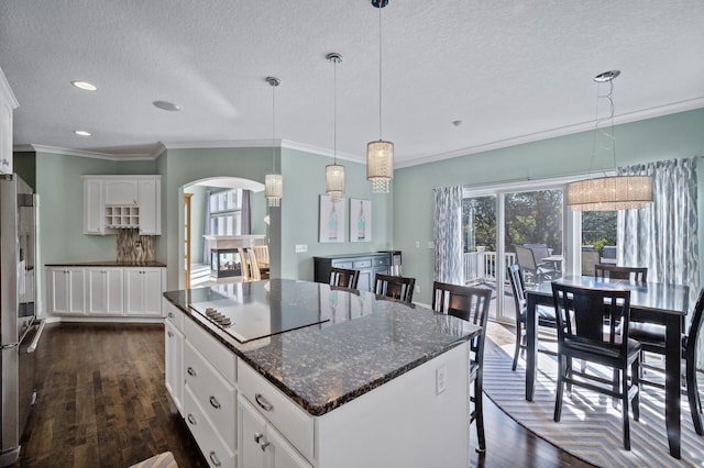 kitchen with a textured ceiling, crown molding, dark wood-style flooring, arched walkways, and a center island