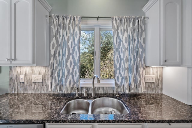 kitchen featuring white cabinets, decorative backsplash, dark stone counters, and a sink