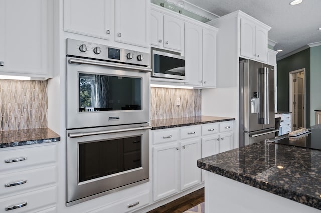 kitchen with dark stone countertops, appliances with stainless steel finishes, ornamental molding, and white cabinetry