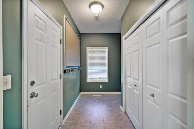 doorway to outside with tile patterned flooring, a textured ceiling, and baseboards