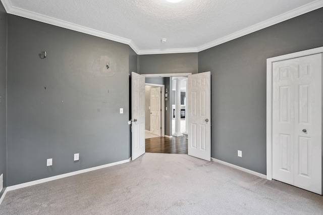 unfurnished bedroom with a closet, a textured ceiling, crown molding, carpet floors, and baseboards