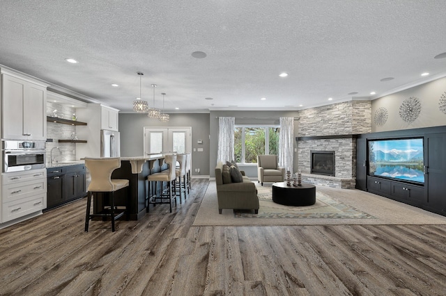 living area featuring recessed lighting, dark wood finished floors, a stone fireplace, and a textured ceiling