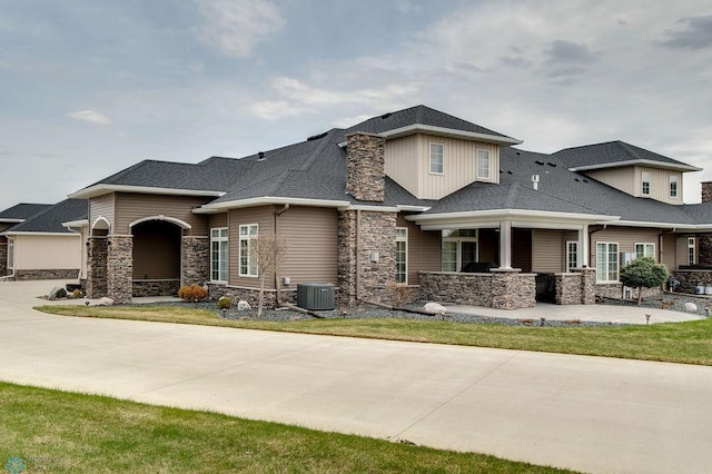 view of front of house featuring central AC unit, stone siding, and roof with shingles