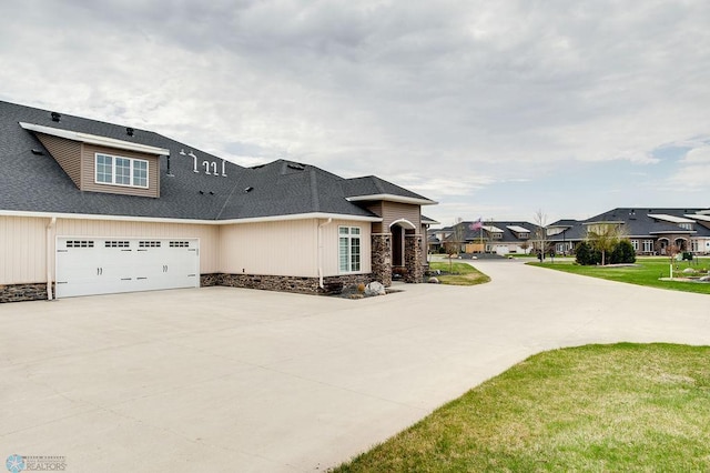 view of front of house with roof with shingles, an attached garage, stone siding, a residential view, and concrete driveway