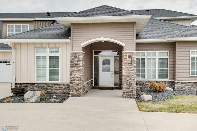 property entrance featuring stone siding, a shingled roof, an attached garage, and board and batten siding