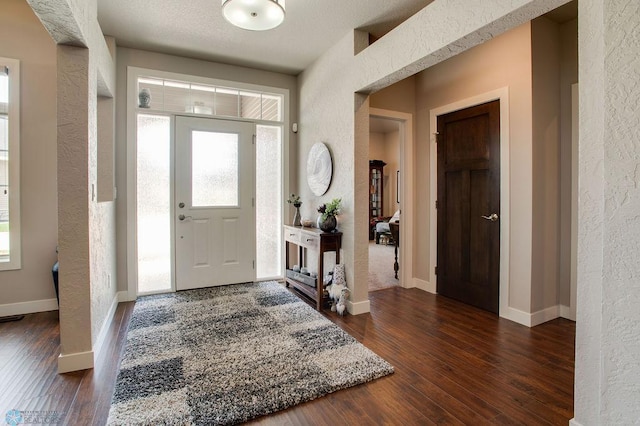 entrance foyer with dark wood finished floors, a healthy amount of sunlight, and a textured wall