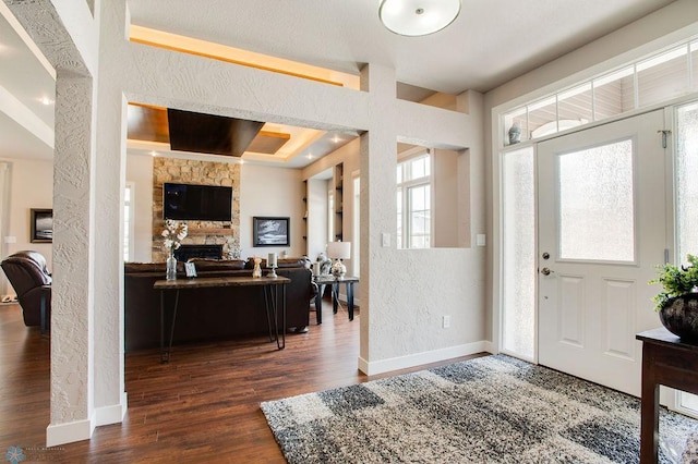 foyer entrance featuring baseboards, a fireplace, a textured wall, and wood finished floors