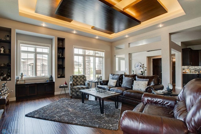 living area with a tray ceiling, hardwood / wood-style flooring, baseboards, and built in shelves