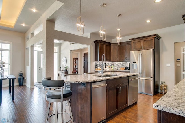 kitchen with light stone counters, dark wood finished floors, a sink, backsplash, and appliances with stainless steel finishes