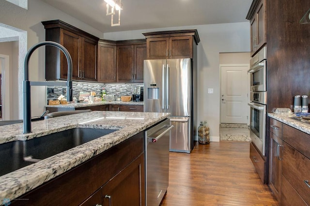 kitchen with a sink, light stone counters, stainless steel appliances, and dark wood-style floors