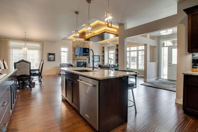 kitchen featuring a sink, dishwasher, a fireplace, open floor plan, and baseboards