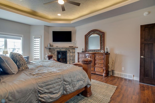 bedroom with a textured ceiling, baseboards, a stone fireplace, visible vents, and wood finished floors