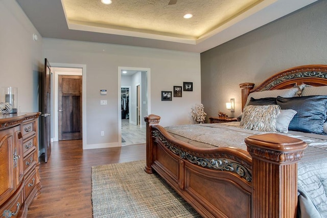 bedroom featuring a tray ceiling, recessed lighting, dark wood finished floors, and a textured ceiling