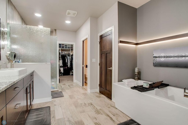 full bath featuring wood finished floors, a walk in closet, a bath, baseboards, and vanity