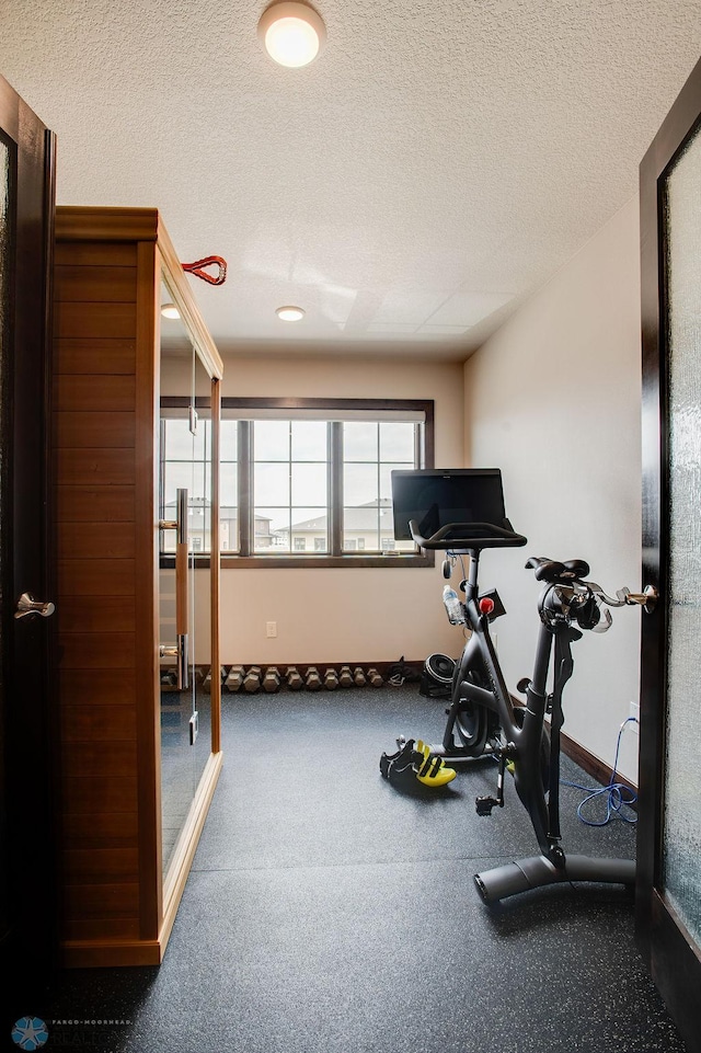 exercise room with a textured ceiling and baseboards