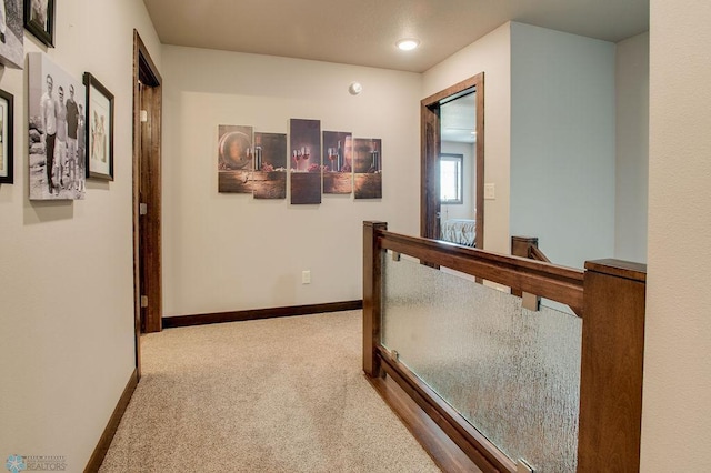 hall with carpet, baseboards, and an upstairs landing