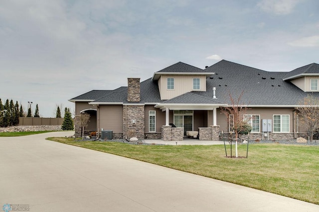 view of front of property featuring a chimney, stone siding, central AC unit, and a front lawn