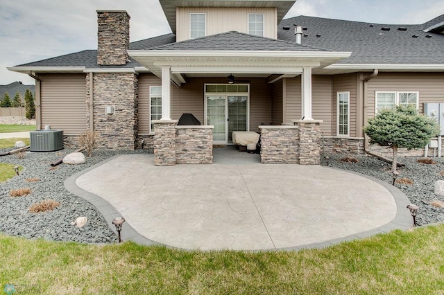 rear view of property with stone siding, a patio, a chimney, area for grilling, and roof with shingles