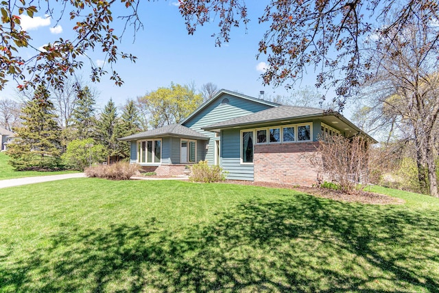 view of front of home with roof with shingles, brick siding, and a front lawn