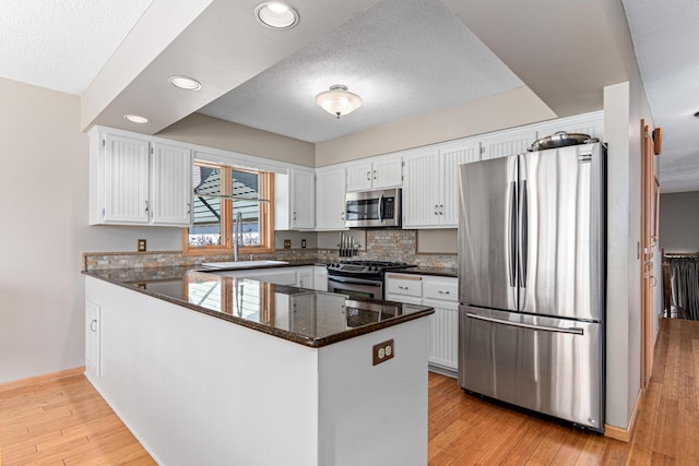 kitchen with a peninsula, a sink, stainless steel appliances, a textured ceiling, and white cabinetry