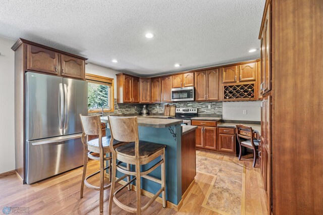 kitchen with stainless steel appliances, a textured ceiling, a kitchen bar, backsplash, and a center island