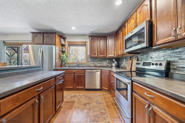 kitchen with appliances with stainless steel finishes, a sink, a textured ceiling, dark countertops, and tasteful backsplash