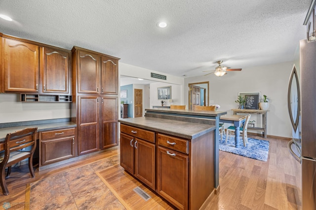 kitchen with freestanding refrigerator, a ceiling fan, dark countertops, a textured ceiling, and light wood-style flooring