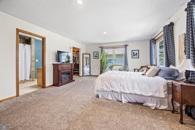 carpeted bedroom featuring a textured ceiling, a glass covered fireplace, a walk in closet, baseboards, and recessed lighting