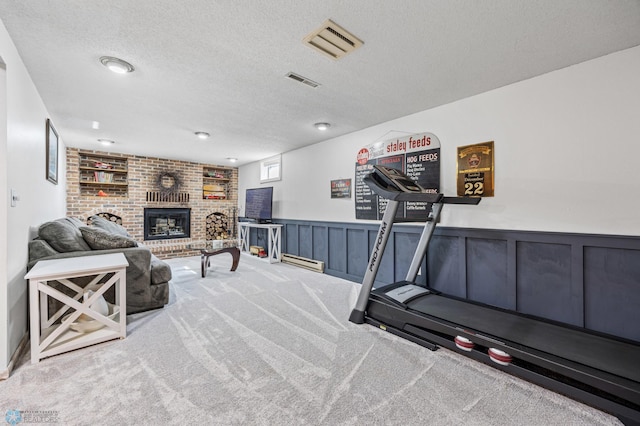 workout room with a textured ceiling, carpet flooring, a fireplace, and a wainscoted wall